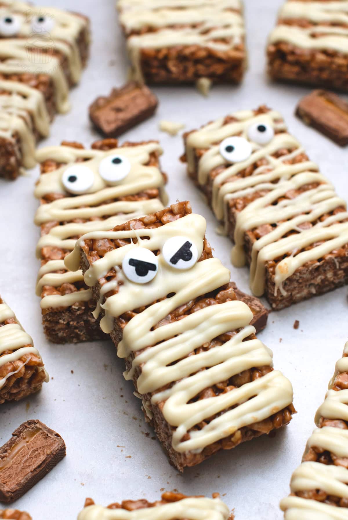 Mummy Mars Bar Slices arranged on greaseproof paper with white chocolate bandages and edible eyes.