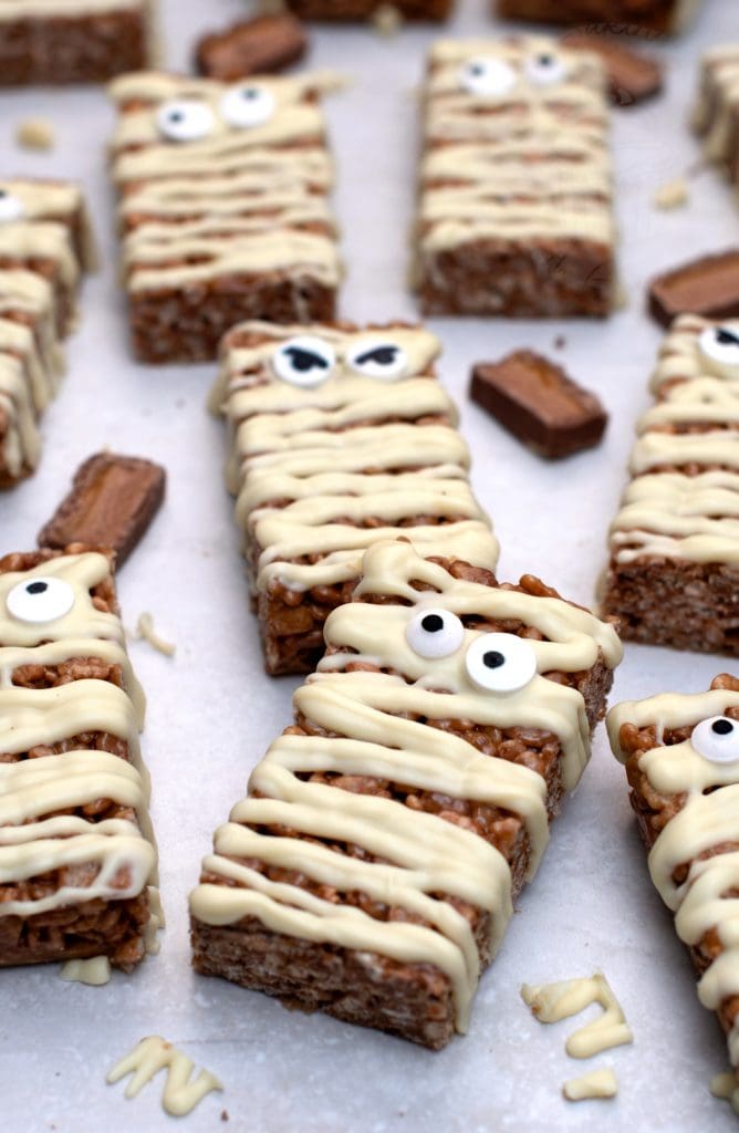Mummy Mars Bar slices decorated with white chocolate bandages and candy eyes, a fun Halloween twist on classic Mars Bar slice.