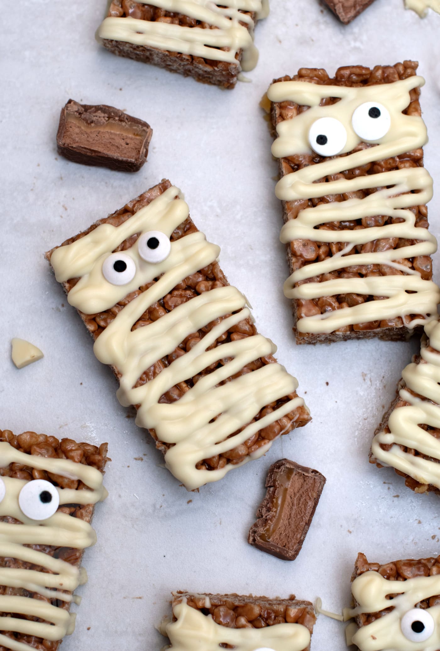 Chocolate Mars Bar slice tray bake cut into mummy shapes with white chocolate bandages and candy eyes.