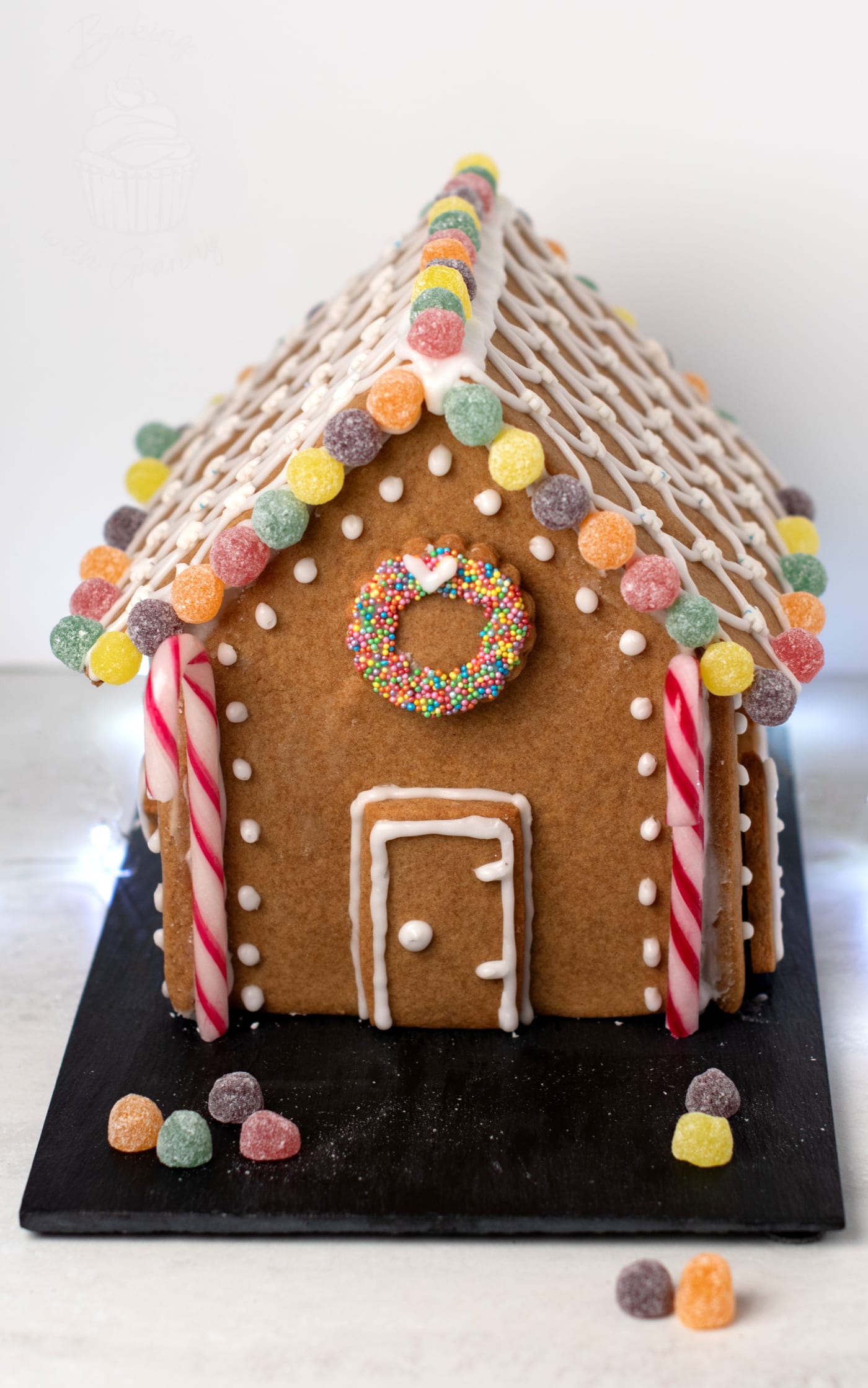 Homemade gingerbread house decorated with royal icing, candy sweets and a biscuit wreath on the front for Christmas.