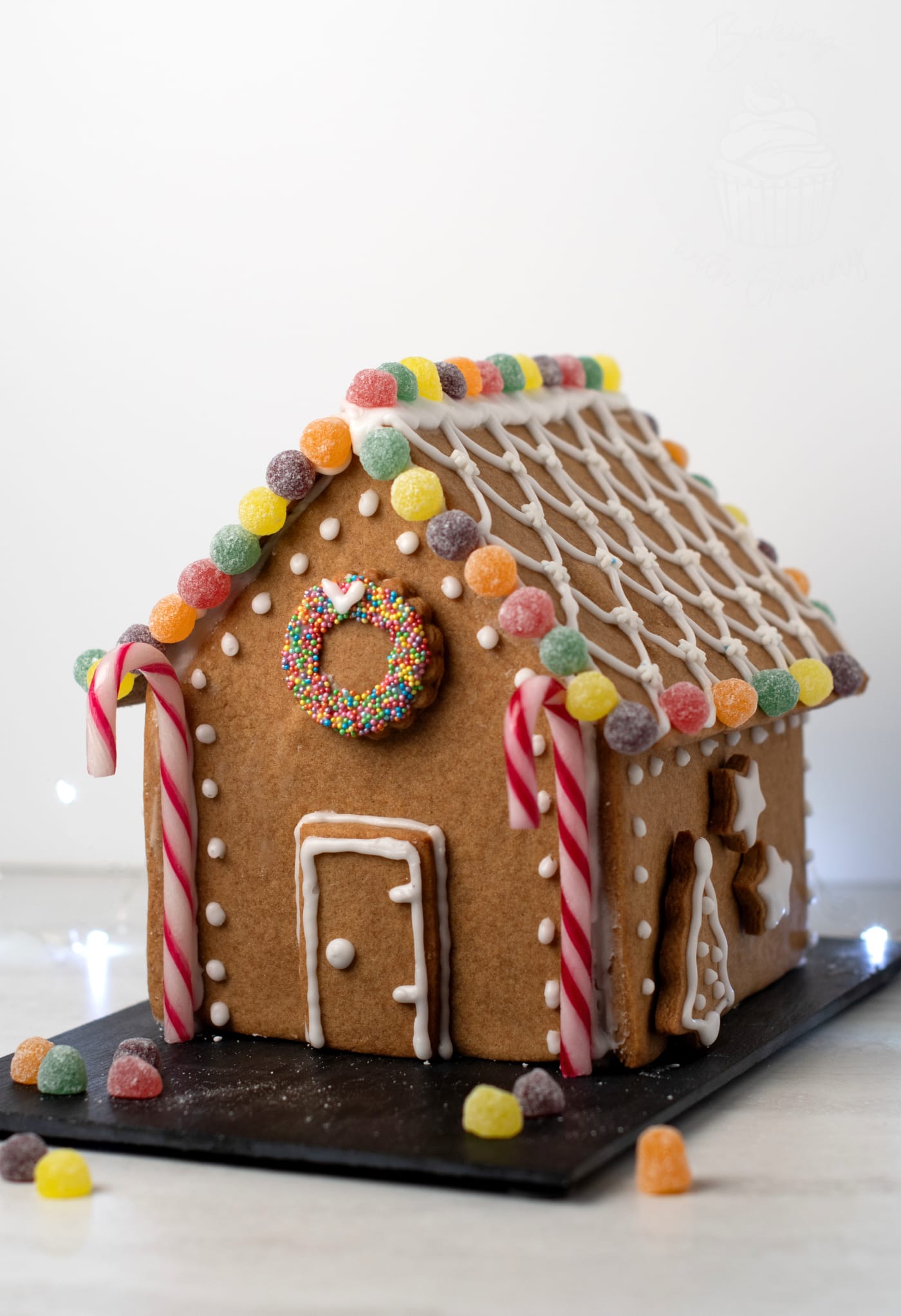 Angle view of a homemade gingerbread house with piped icing roof, candy decorations and candy cane pillars
