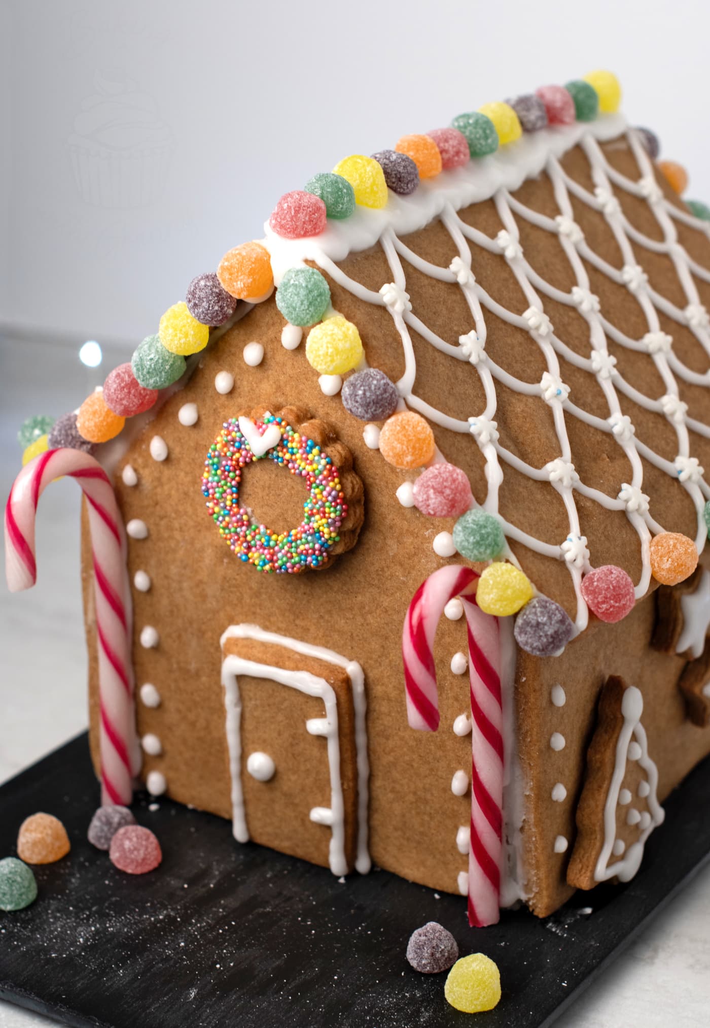 Close-up of a decorated gingerbread house with icing roof pattern, colourful sweets and candy cane supports.