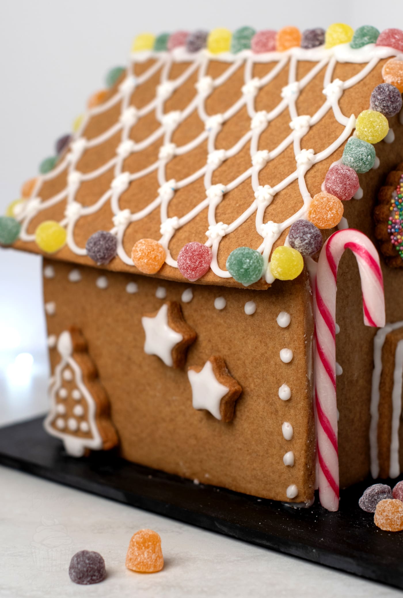 Decorated gingerbread house with piped icing roof tiles and colourful sweets along the roof edge.