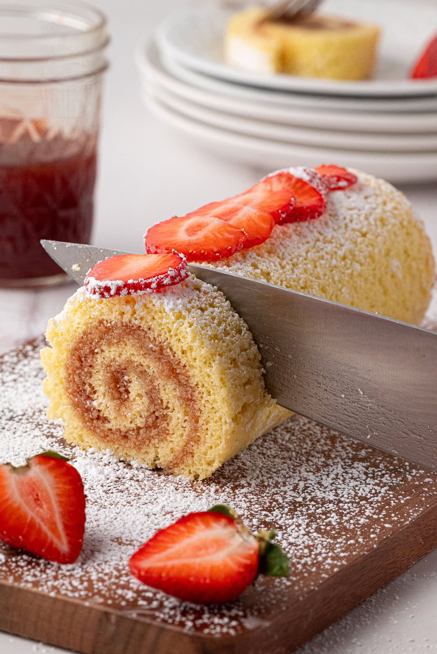 Knife slicing into a homemade jam Swiss roll cake, revealing the light sponge roll and jam swirl.