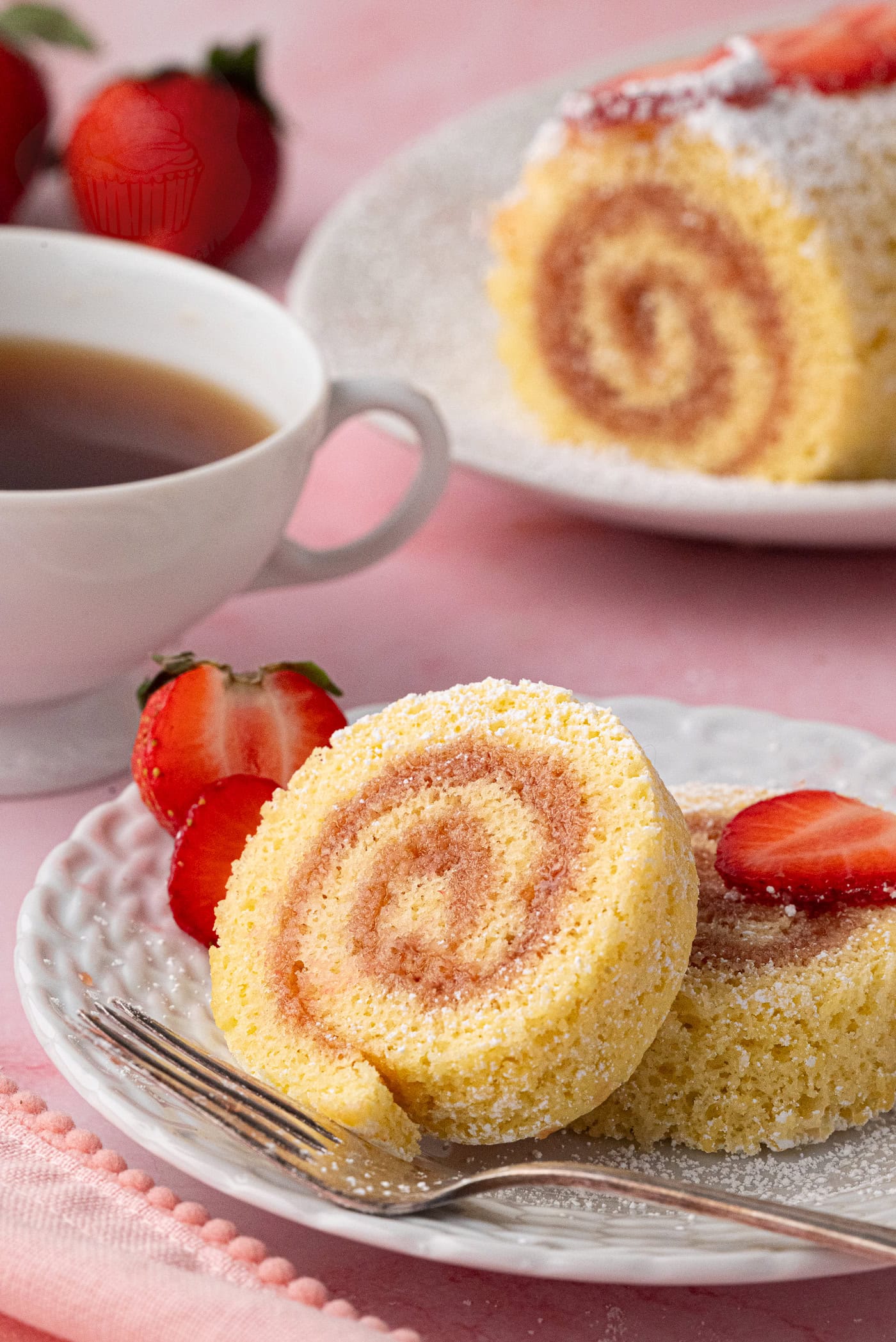 Light and fluffy jam Swiss roll slice dusted with icing sugar, served with fresh strawberries.