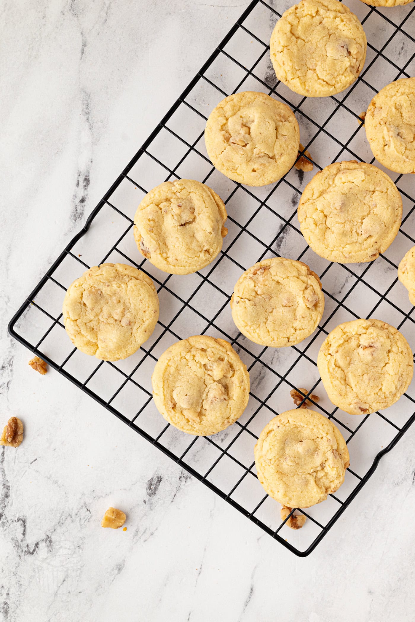 Walnut biscuits cooling on a black wire rack over a marble surface.