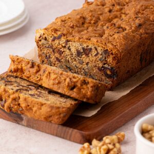 Date and Walnut Loaf on a wooden chopping board, with a couple of slices cut from the end, showing the fruit and nuts inside.