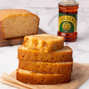 Stack of syrup-drizzled golden syrup cake slices with a bottle of golden syrup in the background.
