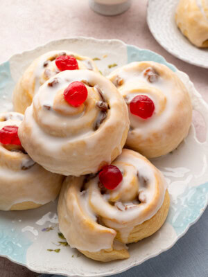 Stack of glazed Belgian buns with red cherries on top, served on a patterned plate, ideal for British teatime.