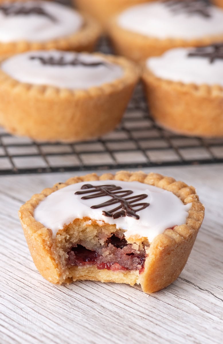 Close-up of a bitten Fern Cake tart showing layers of jam and almond frangipane, topped with white icing and chocolate feathering.