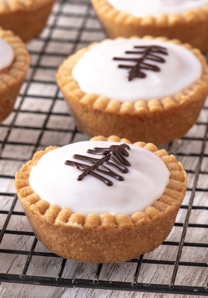 Individual Fern Cake in focus, with other homemade tarts softly blurred in the background on a wire rack.