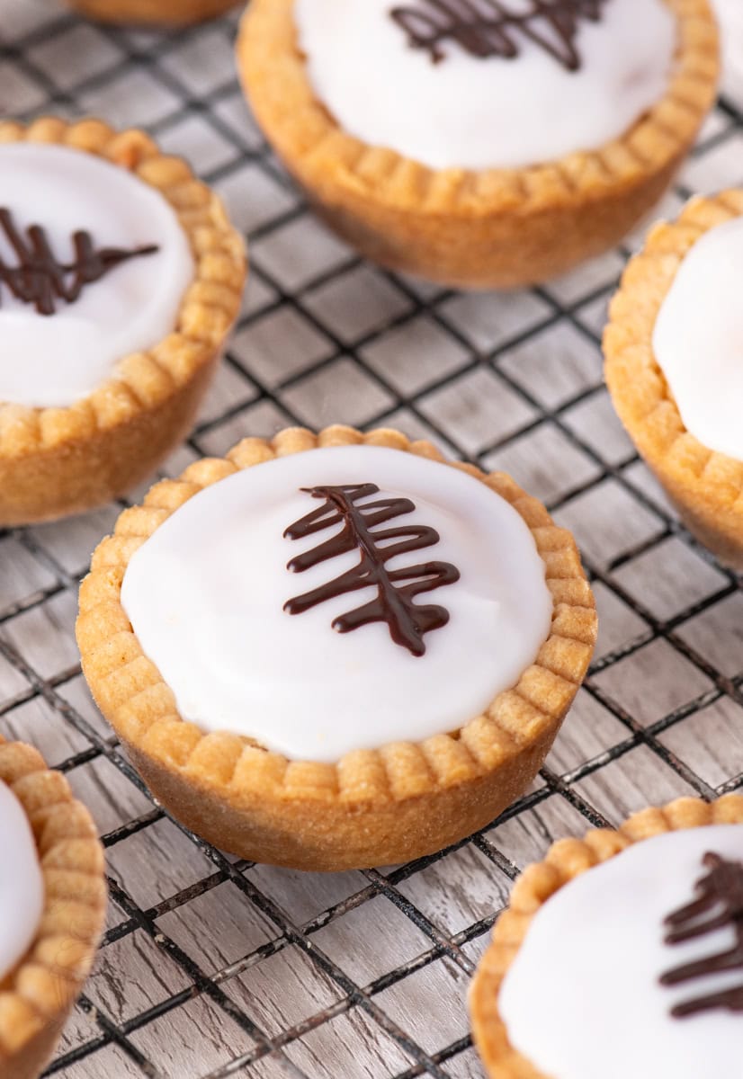 Angled view of multiple Scottish Fern Cake tarts, highlighting the crisp pastry and white glossy icing with chocolate fern detail.