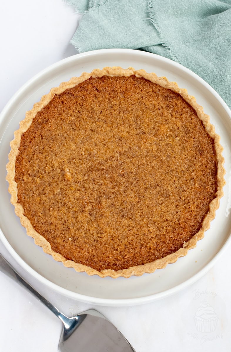 Overhead view of a full treacle tart in a white dish. A simple, old-fashioned British recipe with a golden, sticky filling.