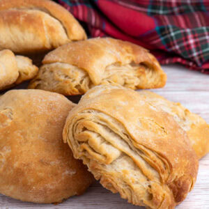 Pile of homemade Scottish butteries (rowies) with tartan cloth in background.
