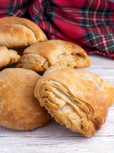 Pile of homemade Scottish butteries (rowies) with tartan cloth in background.