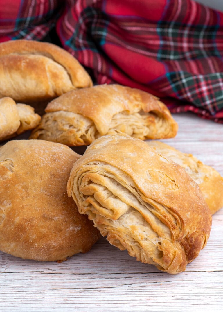 Pile of homemade Scottish butteries (rowies) with tartan cloth in background.