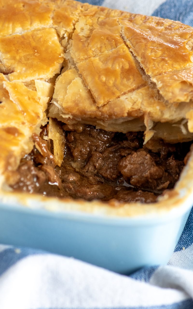 Traditional steak pie recipe with tender beef in gravy under a flaky pastry lid, served in a blue dish.