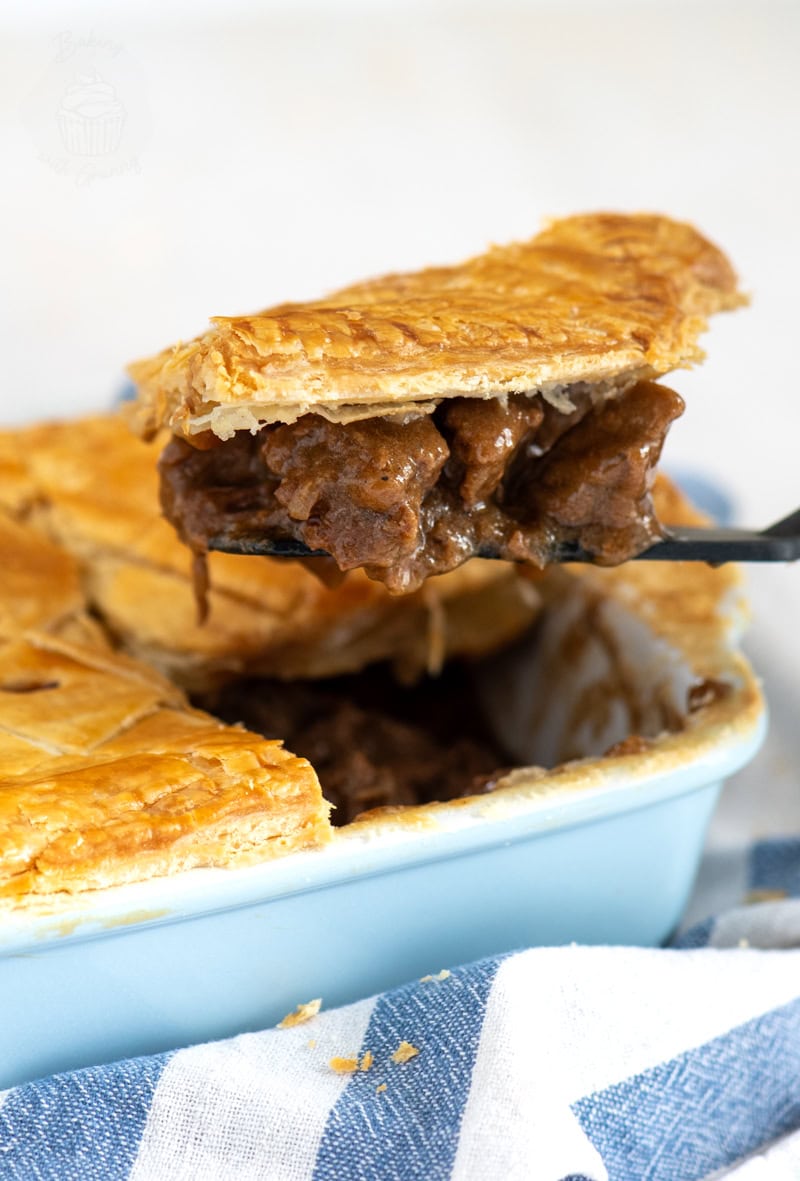 Slice of Scottish steak pie being lifted from the dish, showing chunks of beef in thick gravy.