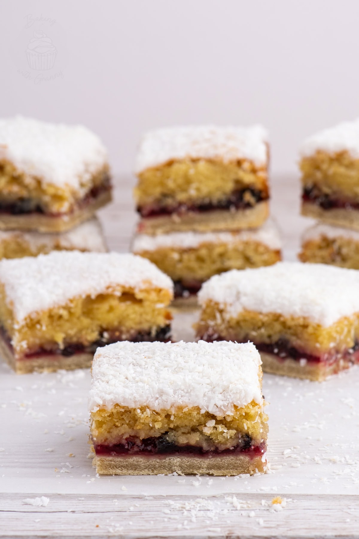 Close-up of a Scottish Snow Cake square showing layers of pastry, raspberry jam, sponge, and coconut icing.