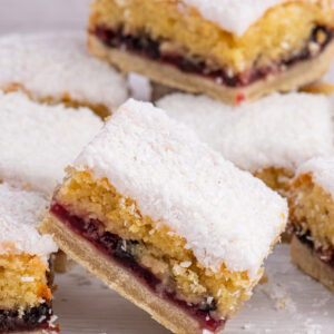 Scottish Snow Cake slices stacked on a white surface, showing the jam and sponge layers beneath a dusting of coconut.