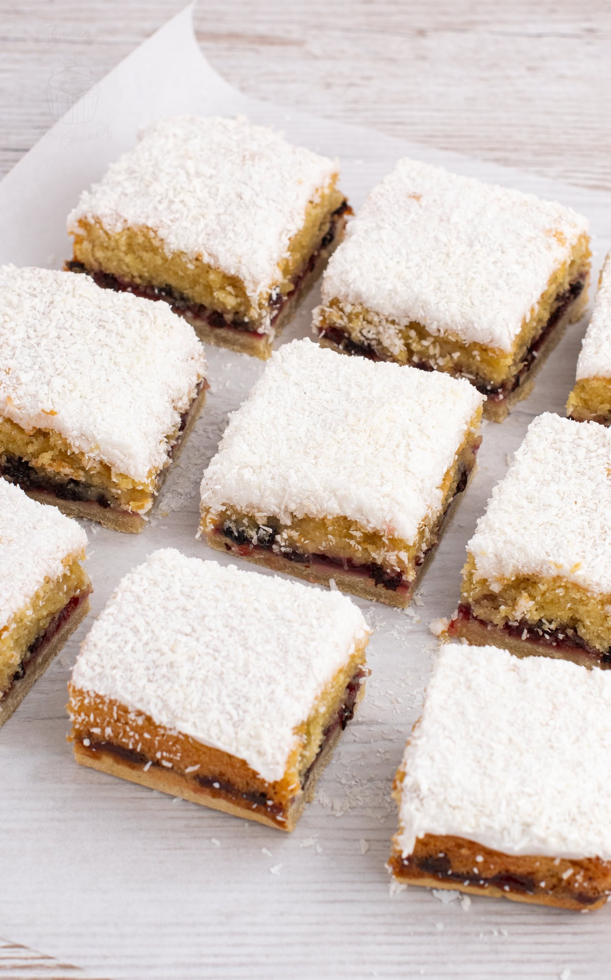 Tray of Scottish Snow Cake cut into squares with visible layers of pastry base, jam filling, sponge cake, and white coconut topping.