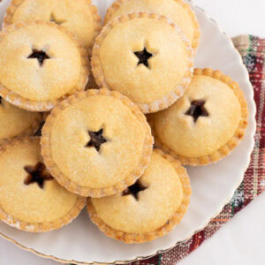 Plateful of classic mince pies arranged on a white dish with festive cloth beneath, perfect for homemade Christmas baking.