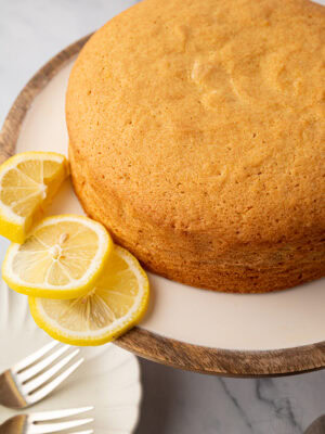Golden Madeira cake on a cake stand styled with sliced lemons on a marble surface.