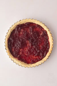 Blind-baked shortcrust pastry case spread with raspberry jam ready for the custard filling in a homemade Manchester Tart recipe.