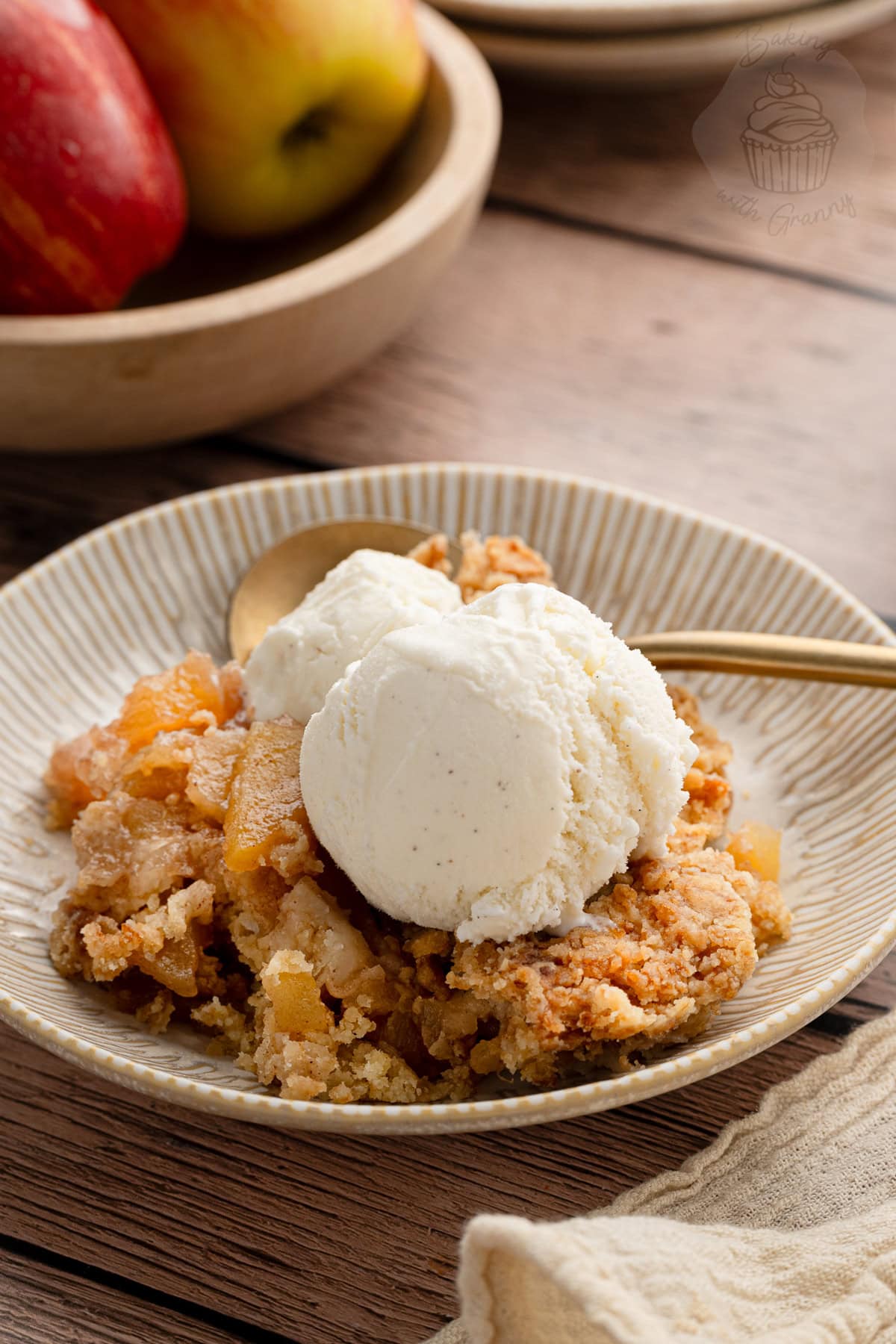 Serving of apple crumble topped with vanilla ice cream on a ceramic plate.