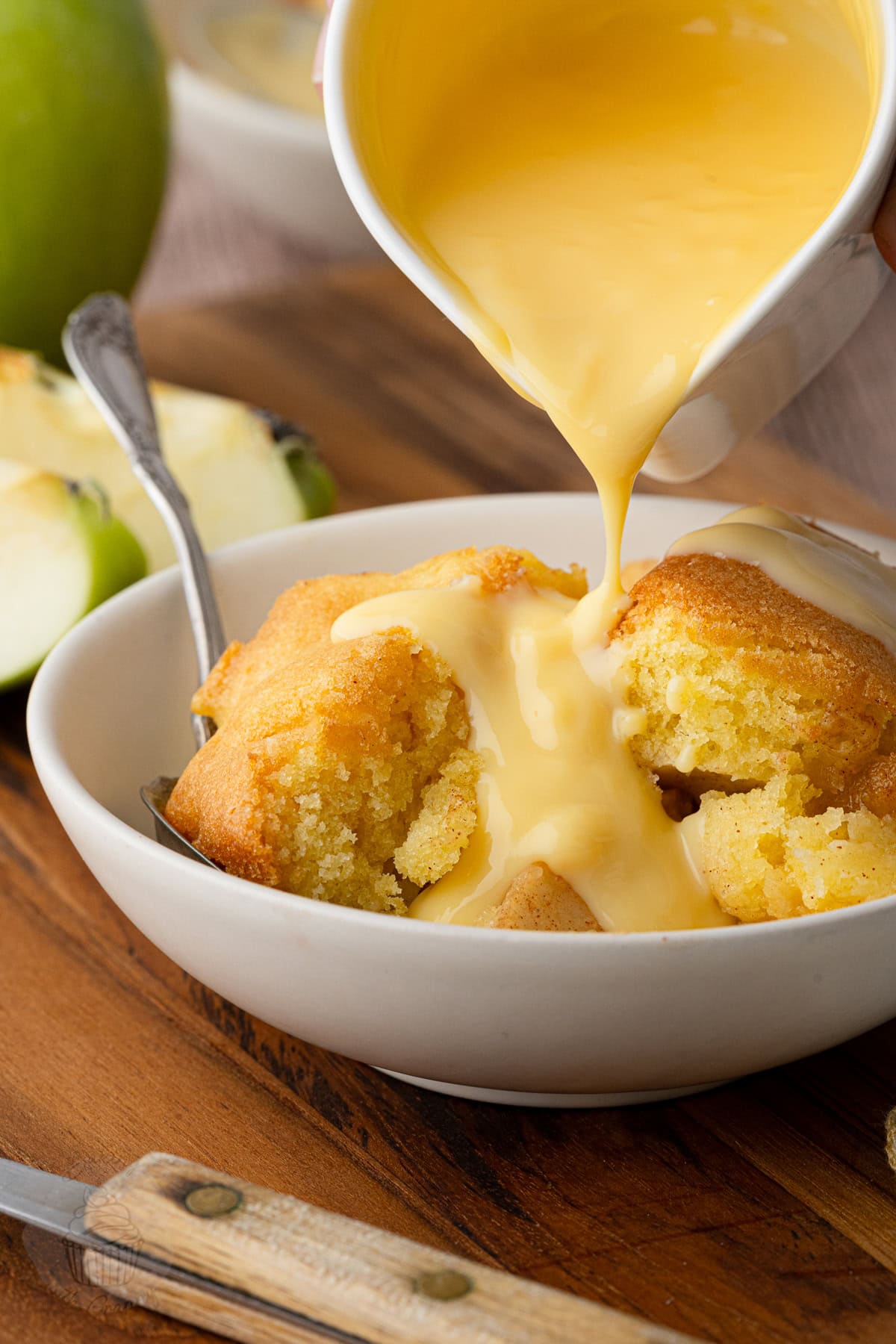 Warm Eve’s Pudding with custard being poured over the apple and sponge.