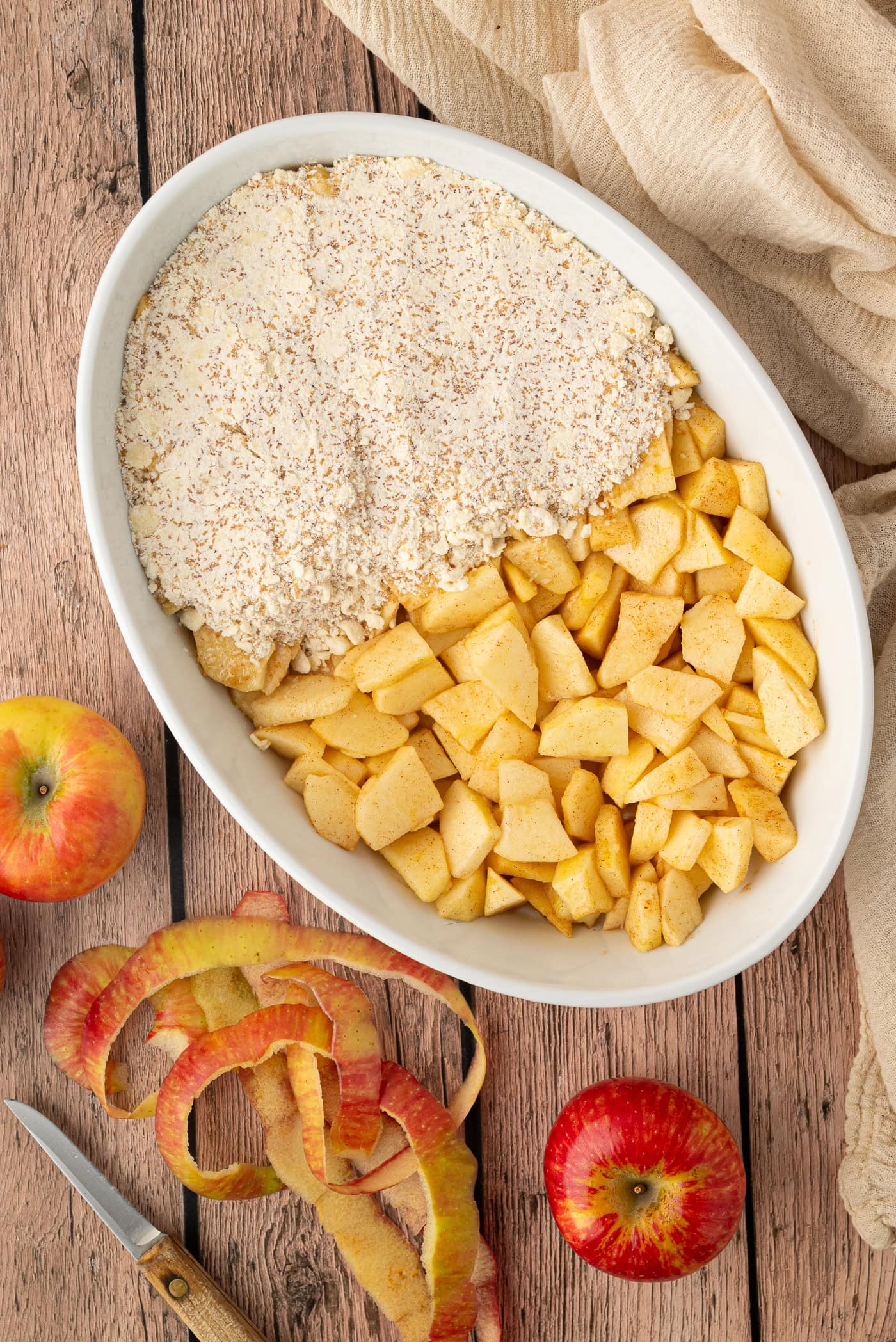 Chopped apples and crumble topping arranged side by side in a white baking dish.