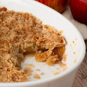 Apple crumble with a portion removed, showing apple pieces beneath the crumble topping.