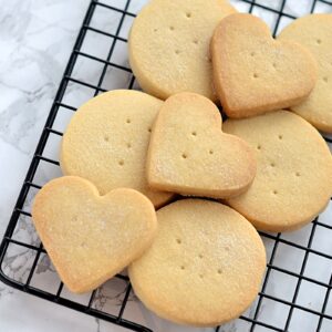 Stack of round and heart-shaped Scottish Shortbread biscuits with more cooling on a rack.