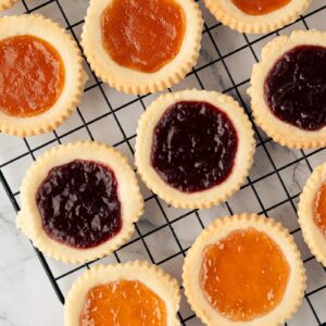 Homemade jam tarts filled with raspberry and apricot jam on a wire cooling rack.