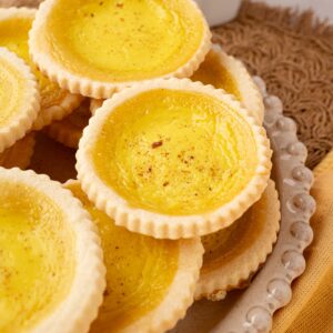 Custard tarts piled on top of one another on a rustic plate.