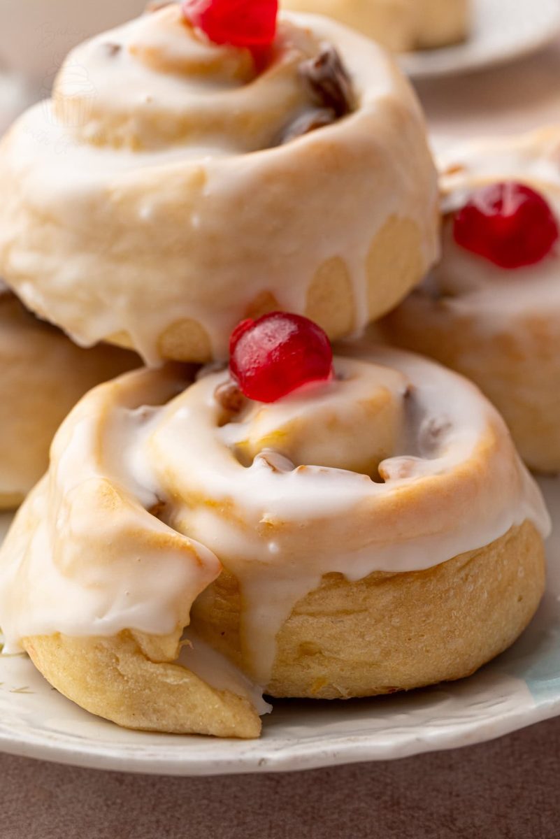 Side view of stacked Belgian buns on a floral plate, highlighting their soft texture and shiny icing glaze.