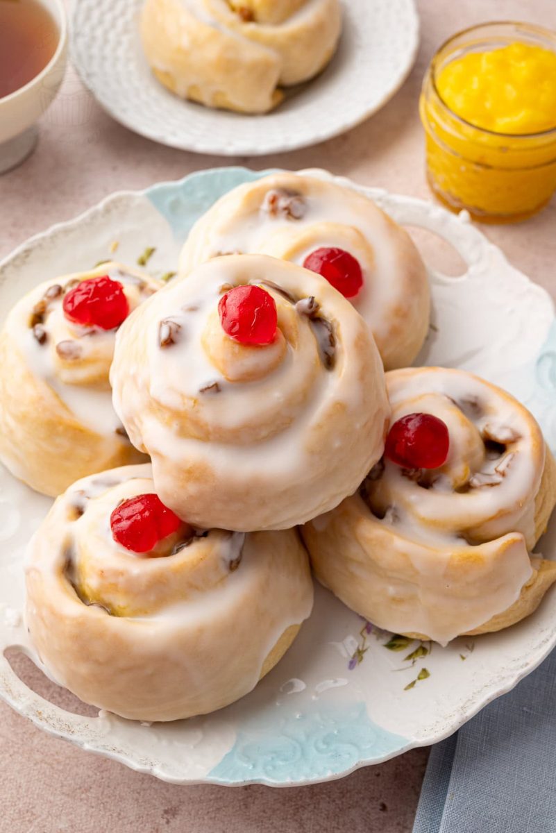 Selection of Belgian buns on a plate, surrounded by a cup of tea and a jar of yellow lemon curd.