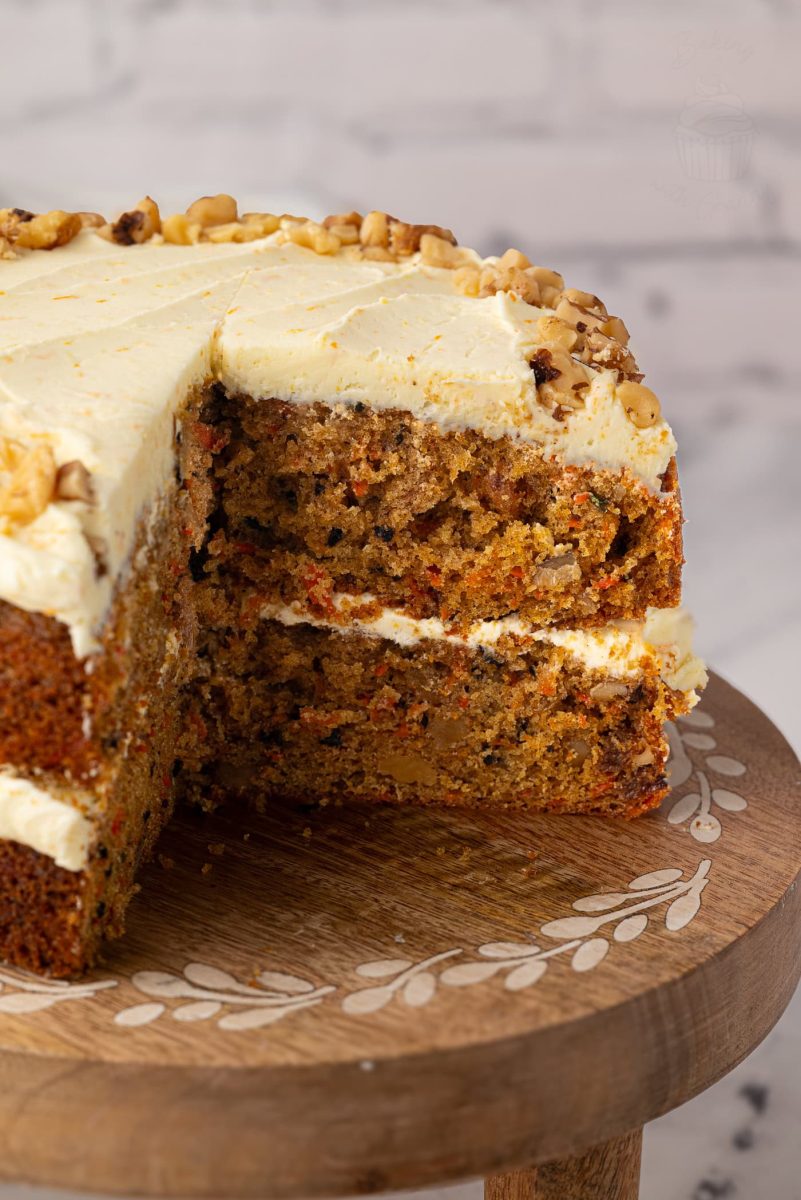 Close-up of the inside of a carrot cake, showing its soft texture and chunks of walnut and carrot, with creamy frosting between the layers and on top.