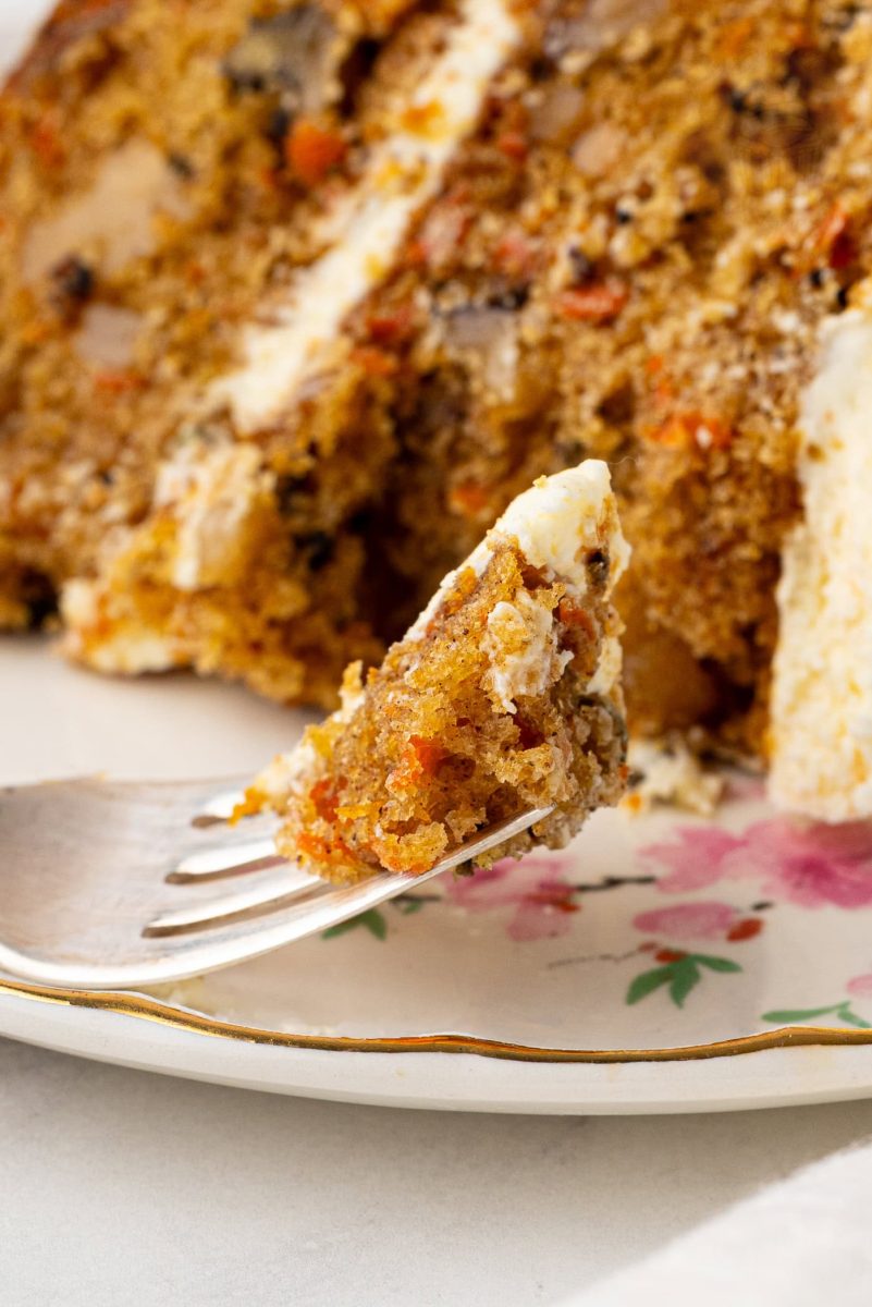 Slice of carrot cake on a plate, with a fork holding up a bite, showcasing the moist crumb and pieces of walnut and carrot.
