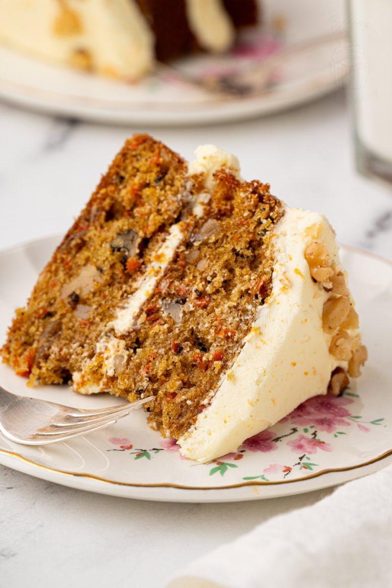 Close-up of a slice of carrot cake with buttercream icing, highlighting the cake's rich texture and chunks of nuts.