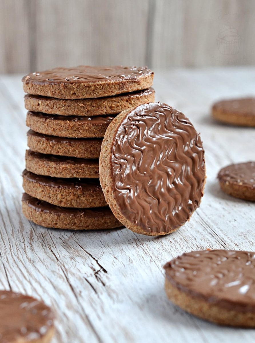A tall stack of British chocolate digestive biscuits, with one cookie resting in front to display the rich chocolate coating and crumbly edge.