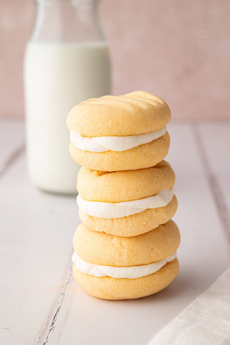 Stack of four custard cream biscuits with bottle of milk in the background.