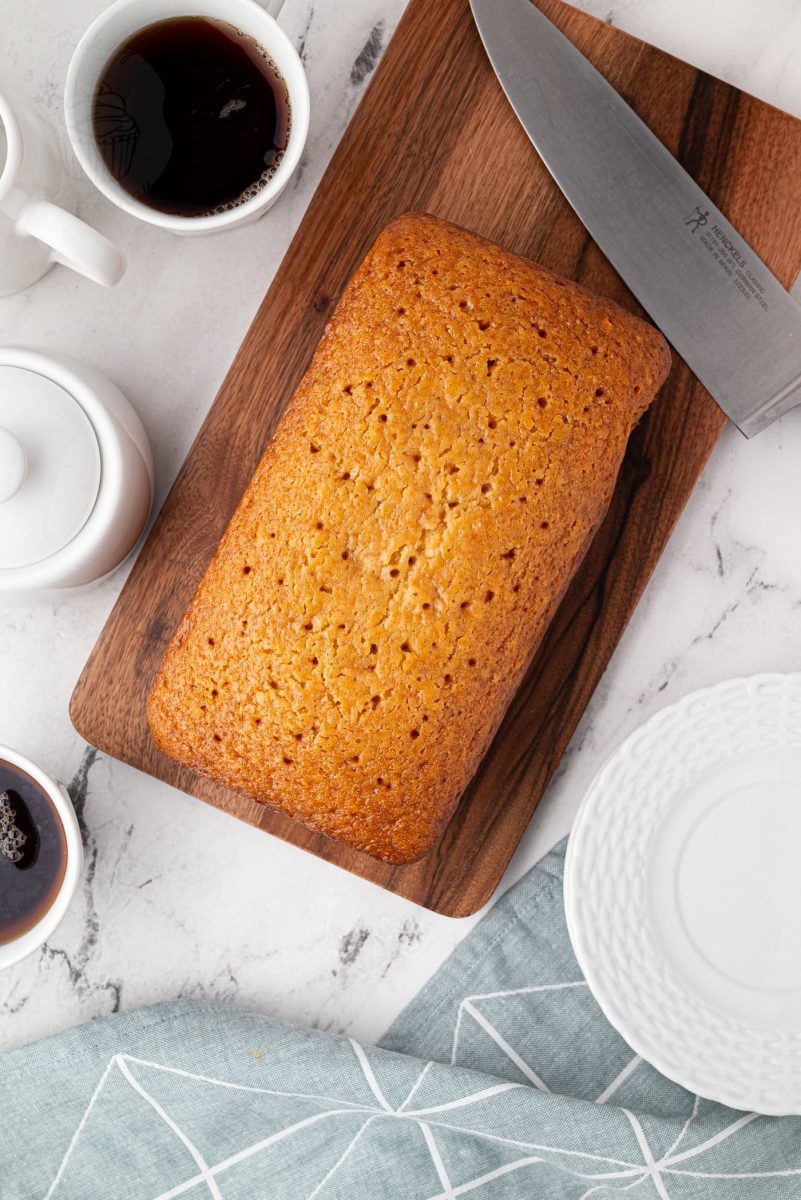 Overhead view of whole golden syrup cake with coffee and plates around it.