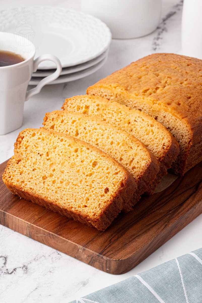 Sliced loaf of golden syrup cake on a wooden board with coffee cups in the background.