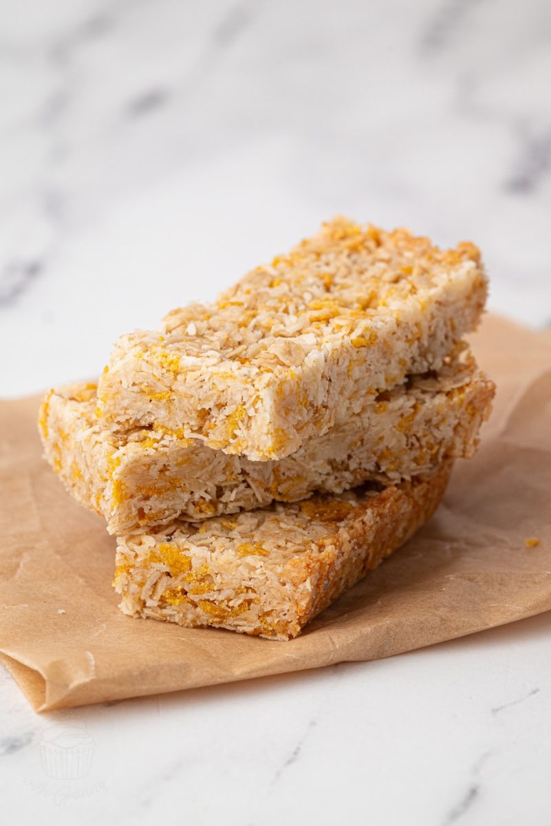 Three honey slice bars stacked on brown parchment paper, showing golden oat texture and neat edges.