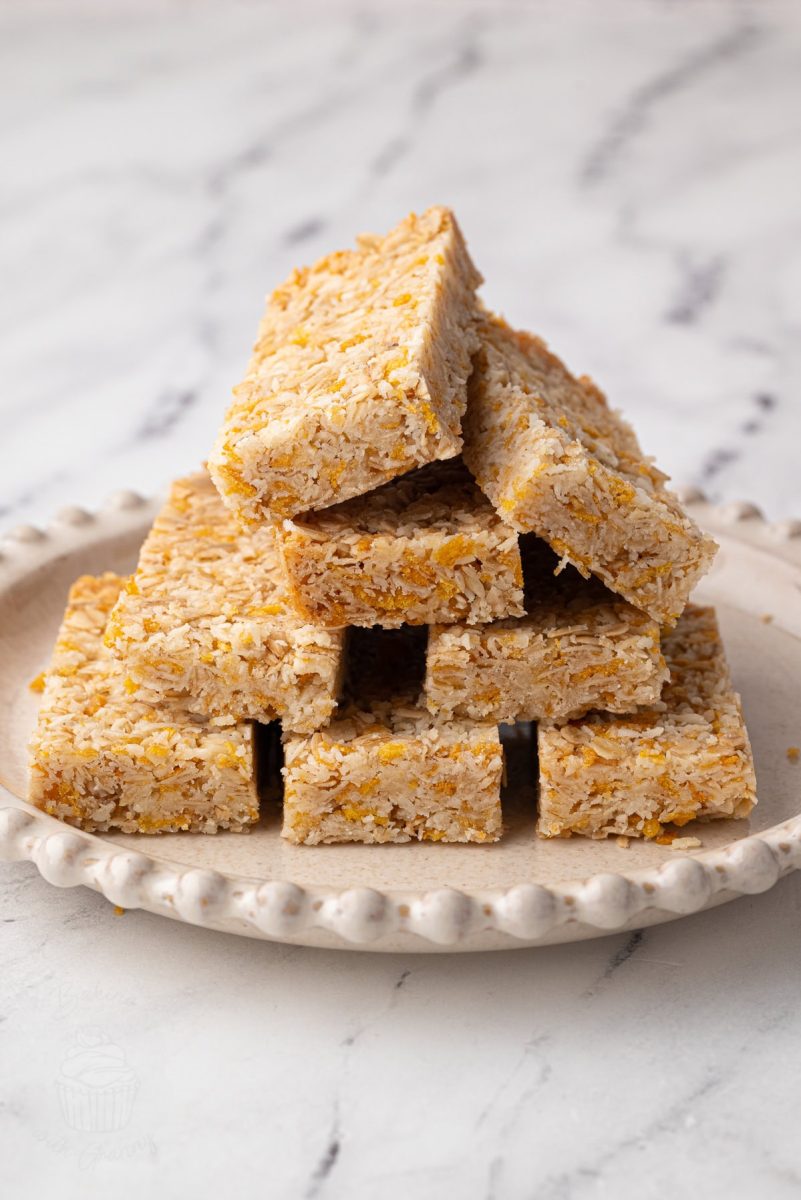 Honey slice bars arranged in a neat stack on a plate with visible layers of oats and coconut.