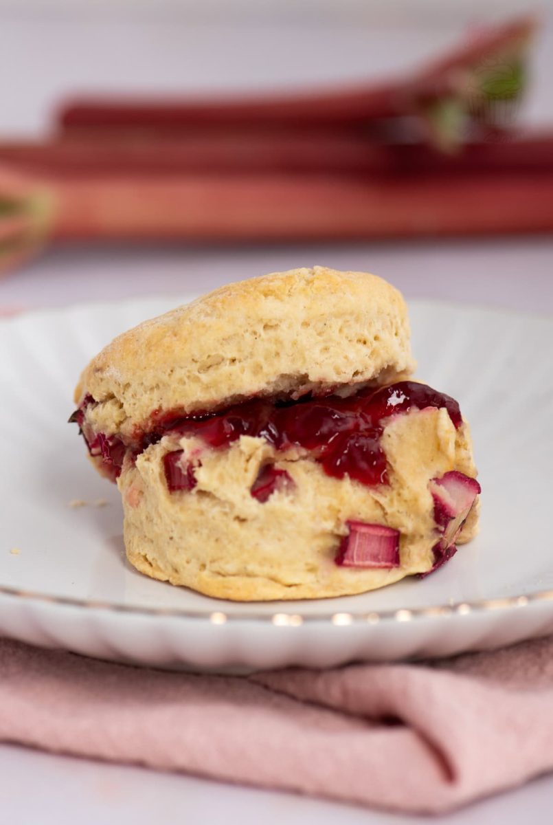 Rhubarb Scone sliced and filled with strawberry jam, served on a white plate with pink napkin.