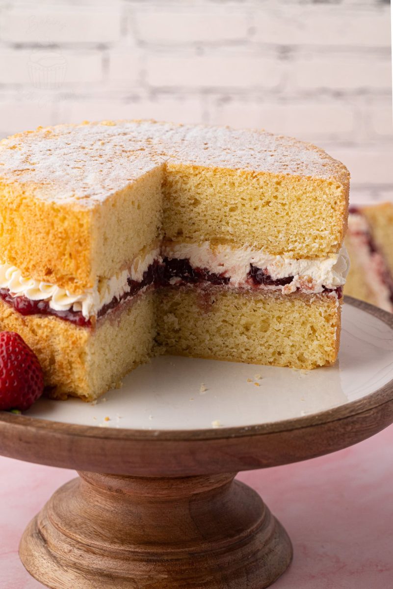 Close-up of a classic Victoria Sponge cake on a wooden cake stand, dusted with caster sugar and filled with strawberry jam and buttercream.