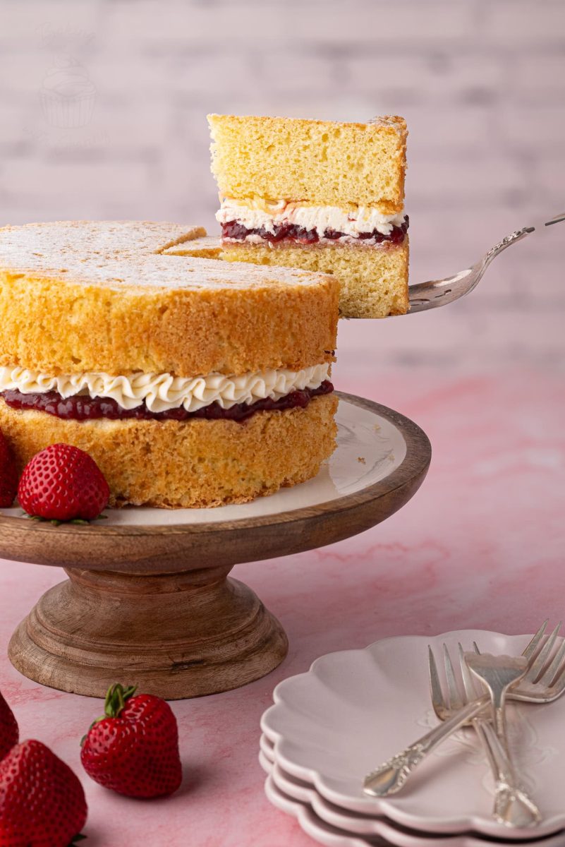 A slice of Victoria Sponge being lifted from the cake, clearly showing the layers of sponge, jam, and buttercream.